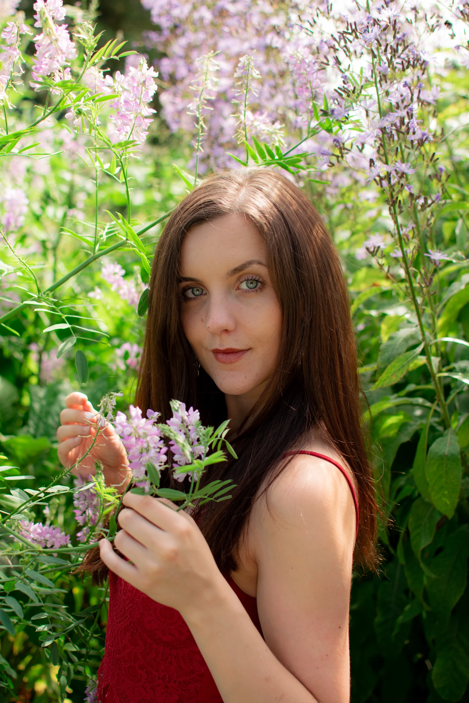 Woman in a red top surrounded by pink flowers and green leaves