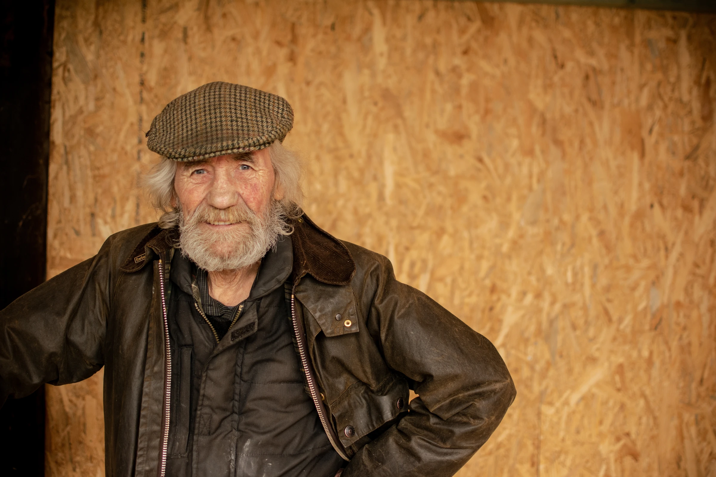 Portrait of a bearded man in a flat cap against a timber wall